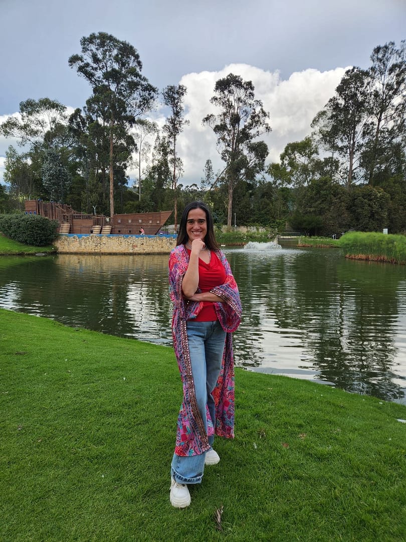 Cata Heincke sonriente junto a un lago y rodeada de árboles, representando presencia amorosa y acompañamiento en procesos de Diseño Humano.